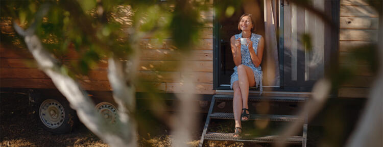 Frau mit Tasse in der Hand sitzt für einem Tiny House
