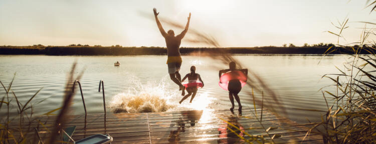 Freunde, die einen Sommertag am See genießen, schwimmen und ins Wasser springen.